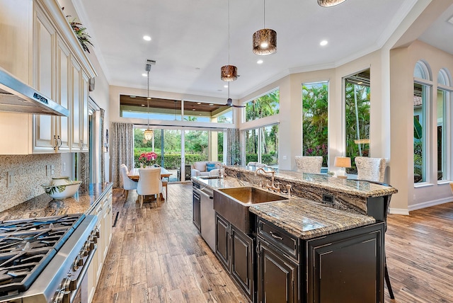 kitchen with backsplash, dark stone counters, wall chimney exhaust hood, light hardwood / wood-style floors, and stainless steel appliances