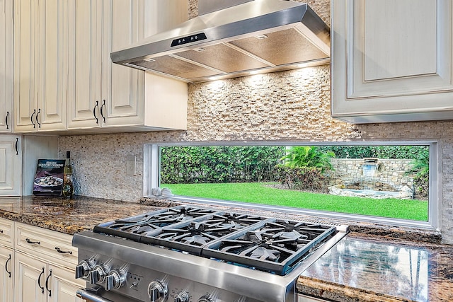 kitchen with tasteful backsplash, stainless steel range, wall chimney exhaust hood, and dark stone counters