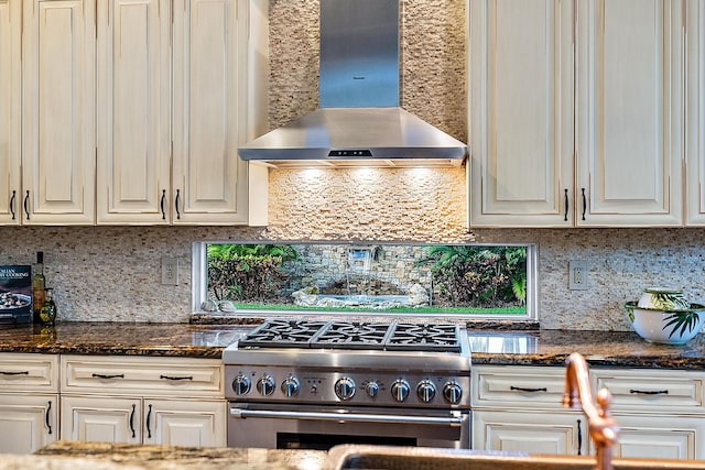 kitchen featuring wall chimney exhaust hood, dark stone counters, high end stainless steel range, and tasteful backsplash