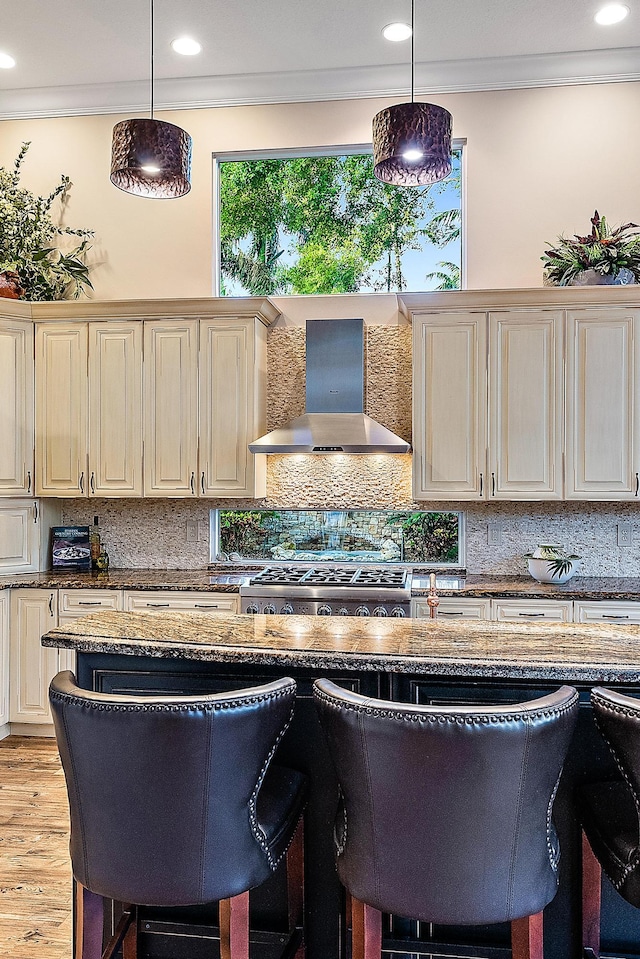 kitchen with pendant lighting, wall chimney range hood, and a breakfast bar area