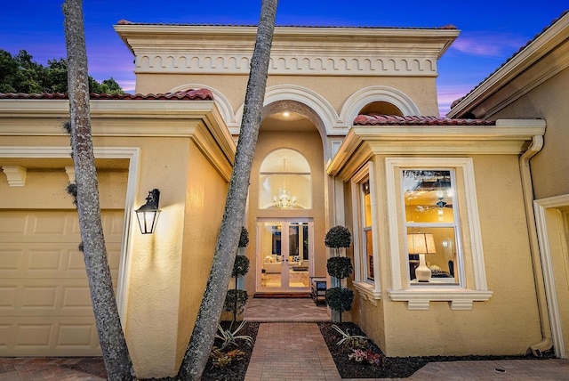 7190 Tradition Cove Ln E, West Palm Beach, FL 33412 - exterior entry at dusk with stucco siding, a garage, a tile roof, and french doors