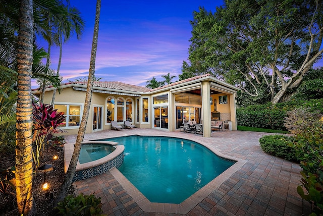 pool at dusk featuring an in ground hot tub and a patio