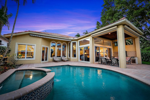 pool at dusk featuring a patio area and an in ground hot tub