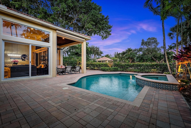 pool at dusk with a patio area and an in ground hot tub