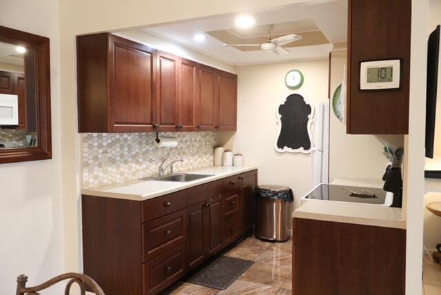 kitchen featuring ceiling fan, sink, stove, a tray ceiling, and decorative backsplash