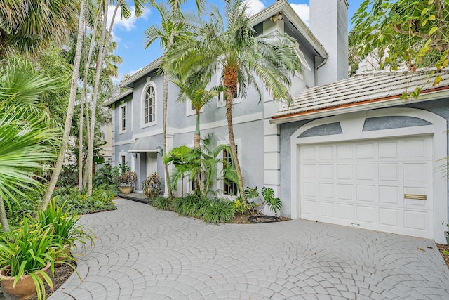 view of front facade featuring stucco siding, decorative driveway, a garage, and a chimney