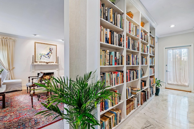 living area featuring wall of books, marble finish floor, a warm lit fireplace, and ornamental molding