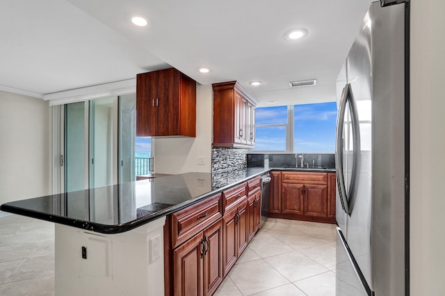 kitchen with kitchen peninsula, appliances with stainless steel finishes, backsplash, dark stone counters, and light tile patterned flooring