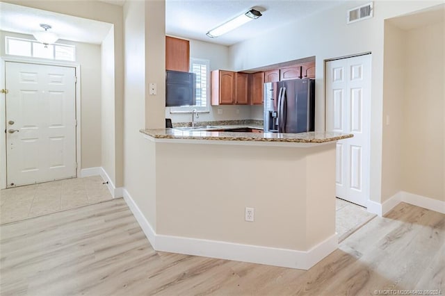 kitchen featuring light hardwood / wood-style flooring, kitchen peninsula, light stone counters, and stainless steel fridge