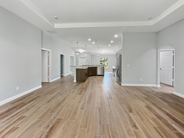 unfurnished living room with sink, a tray ceiling, and light hardwood / wood-style flooring