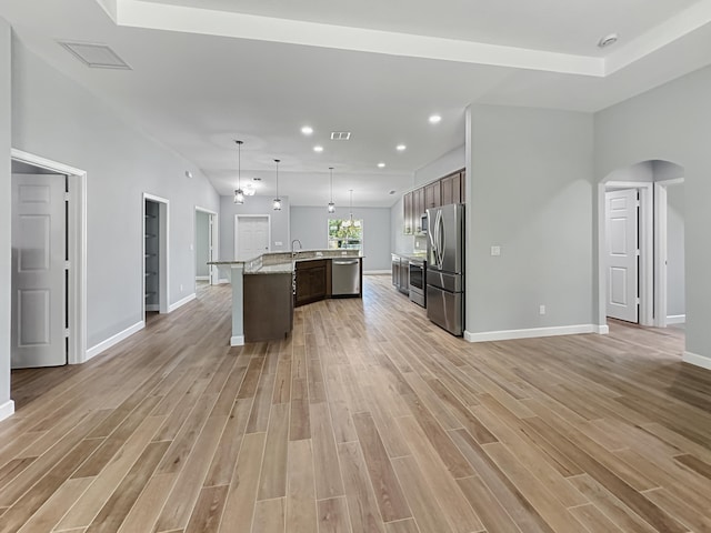 kitchen featuring a center island with sink, light hardwood / wood-style floors, decorative light fixtures, and appliances with stainless steel finishes