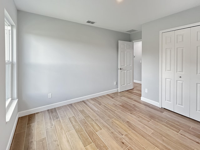 unfurnished bedroom with multiple windows, a closet, and light wood-type flooring