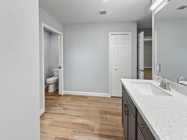 bathroom featuring vanity, toilet, wood-type flooring, and a textured ceiling