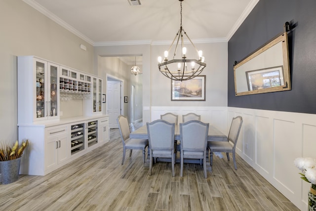 dining room with ornamental molding, indoor bar, a chandelier, and light hardwood / wood-style flooring