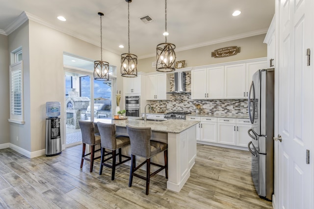 kitchen featuring white cabinetry, wall chimney range hood, stainless steel appliances, and a center island with sink