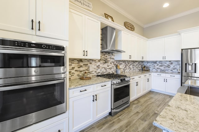 kitchen featuring wall chimney range hood, crown molding, appliances with stainless steel finishes, light stone counters, and white cabinets