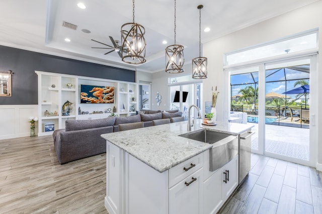 kitchen with white cabinetry, crown molding, light stone counters, hanging light fixtures, and an island with sink