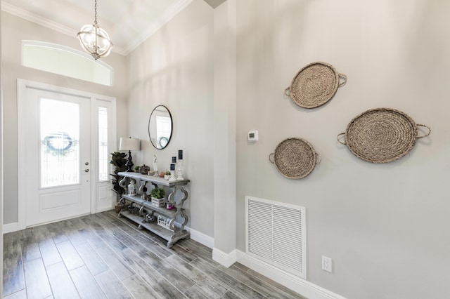 foyer entrance with wood-type flooring, ornamental molding, and a chandelier