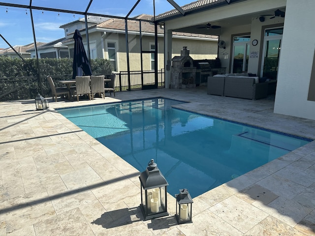 view of swimming pool featuring a lanai, an outdoor living space with a fireplace, ceiling fan, and a patio area