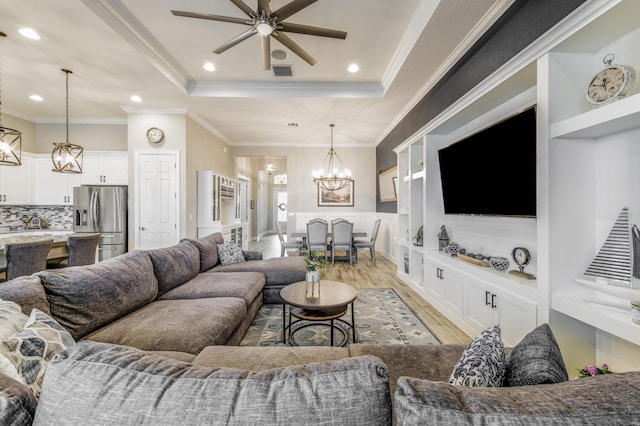 living room featuring ceiling fan with notable chandelier, ornamental molding, a raised ceiling, and light hardwood / wood-style floors