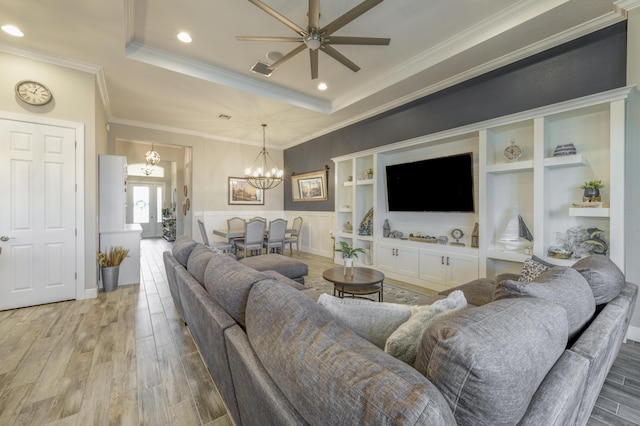 living room featuring crown molding, a tray ceiling, wood-type flooring, and ceiling fan with notable chandelier