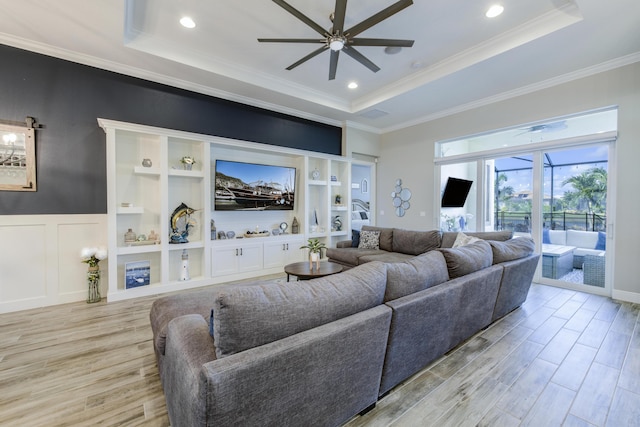 living room featuring crown molding, a tray ceiling, light hardwood / wood-style floors, and ceiling fan