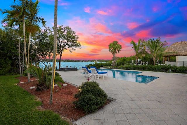 pool at dusk featuring a patio and a water view