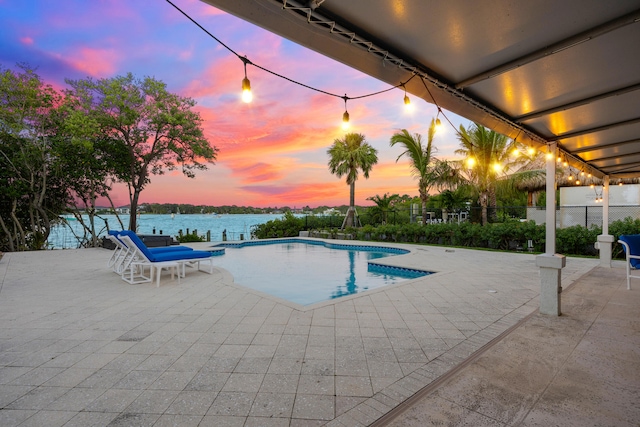 pool at dusk with a patio and a water view