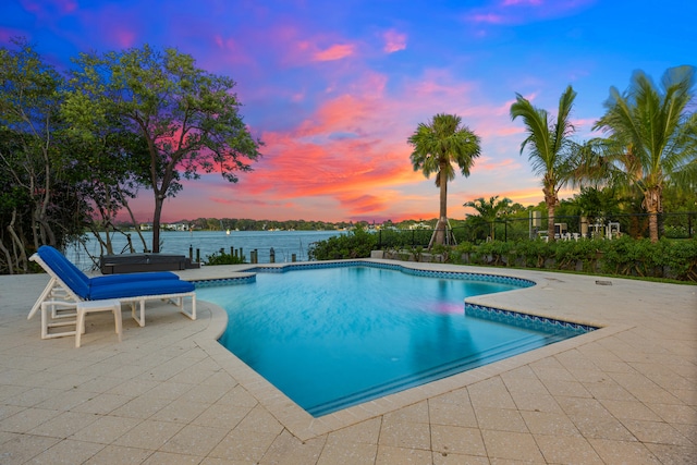 pool at dusk with a water view and a patio area