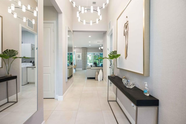 hallway featuring washer / clothes dryer, a notable chandelier, and light tile patterned flooring