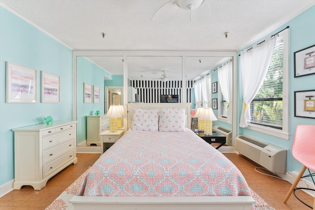 bedroom featuring light wood-type flooring, a textured ceiling, a wall mounted AC, ceiling fan, and crown molding