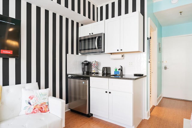 kitchen with appliances with stainless steel finishes, light hardwood / wood-style flooring, white cabinetry, and dark stone counters