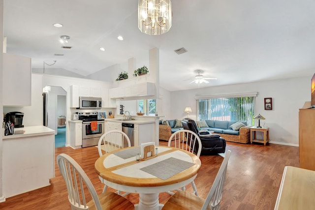 dining area featuring ceiling fan with notable chandelier, light wood-type flooring, sink, and vaulted ceiling