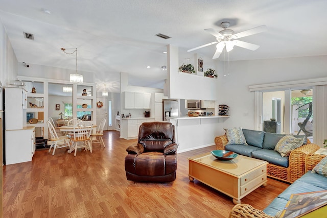 living room featuring ceiling fan with notable chandelier, light hardwood / wood-style flooring, and lofted ceiling