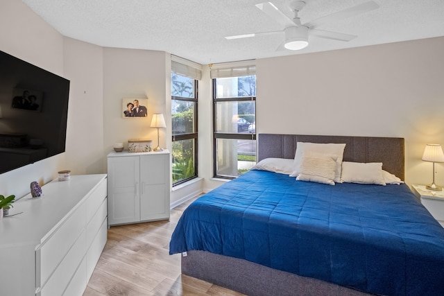 bedroom featuring multiple windows, ceiling fan, a textured ceiling, and light wood-type flooring