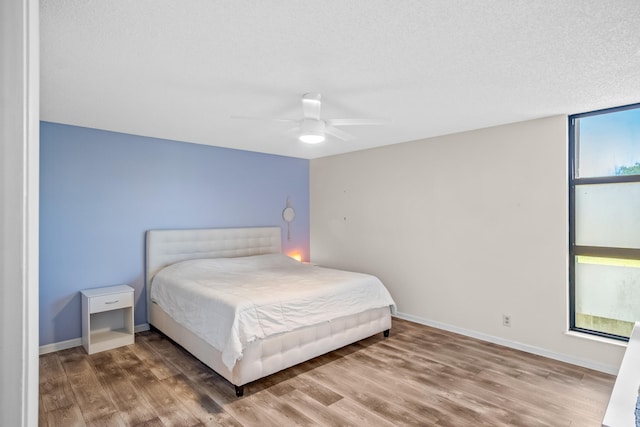 bedroom with ceiling fan, wood-type flooring, and a textured ceiling