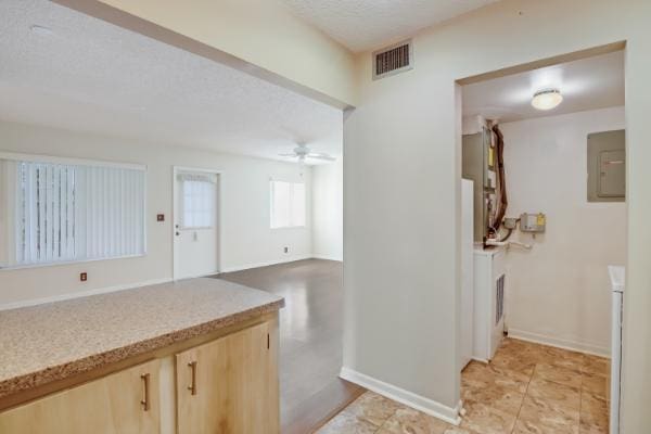 kitchen with ceiling fan, light brown cabinets, a textured ceiling, and electric panel