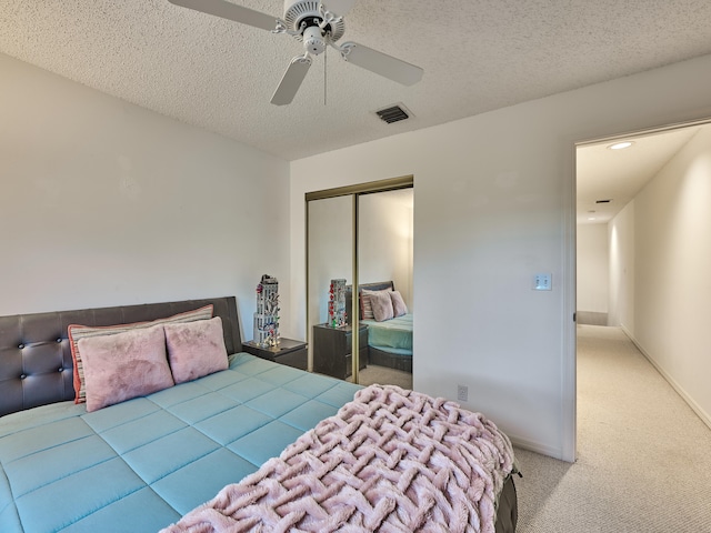 bedroom with ceiling fan, a closet, light colored carpet, and a textured ceiling