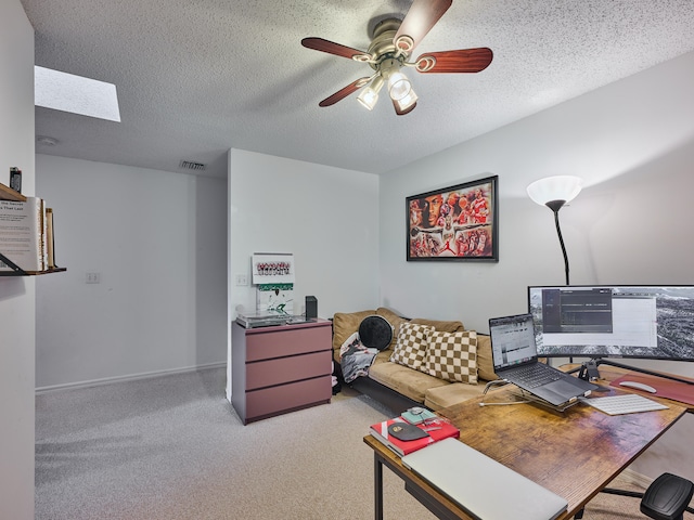 carpeted office featuring a textured ceiling, a skylight, and ceiling fan