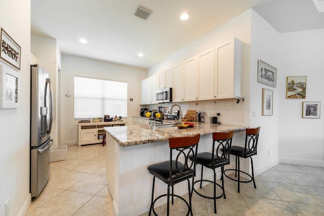 kitchen featuring white cabinetry, light stone countertops, stainless steel appliances, a breakfast bar area, and decorative backsplash