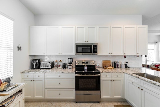 kitchen with a healthy amount of sunlight, light stone counters, white cabinetry, and stainless steel appliances