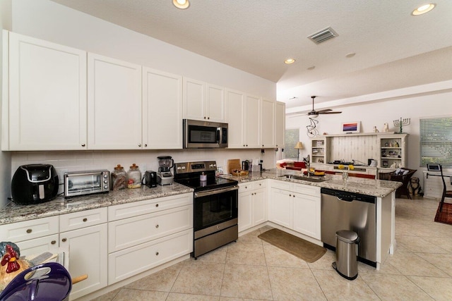 kitchen with kitchen peninsula, light stone countertops, stainless steel appliances, sink, and white cabinetry