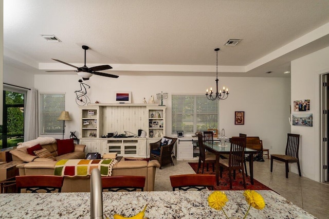 tiled living room with a textured ceiling, ceiling fan with notable chandelier, and a raised ceiling