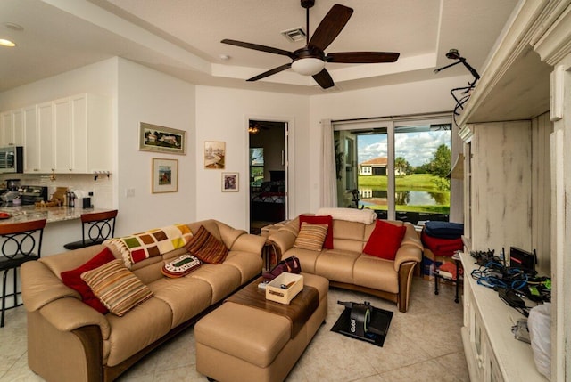 tiled living room with ceiling fan and a raised ceiling