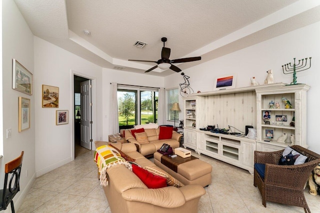 tiled living room with a tray ceiling, ceiling fan, and a textured ceiling