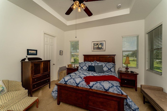 bedroom featuring ceiling fan, a raised ceiling, light colored carpet, and a textured ceiling