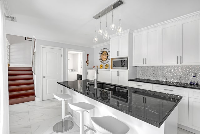 kitchen featuring white cabinetry, stainless steel microwave, a kitchen breakfast bar, dark stone counters, and a center island with sink