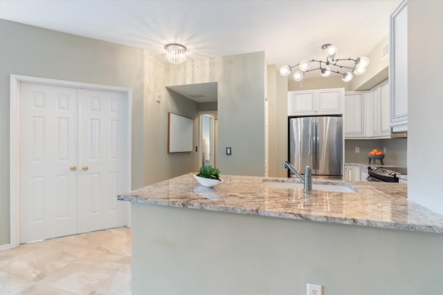 kitchen featuring a peninsula, light stone countertops, freestanding refrigerator, and white cabinetry