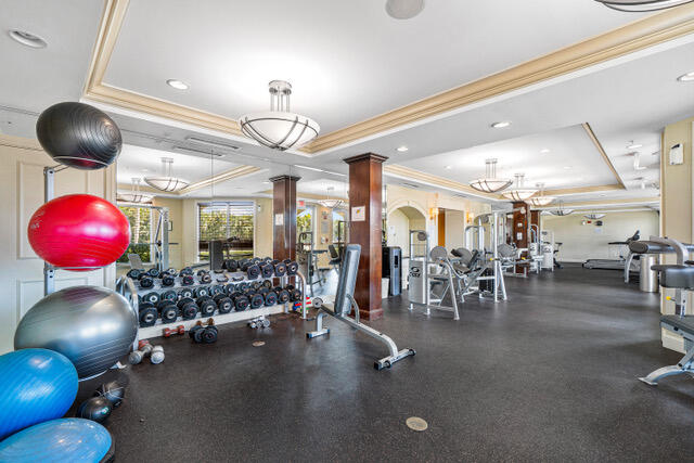 gym with ornate columns, a tray ceiling, crown molding, and recessed lighting