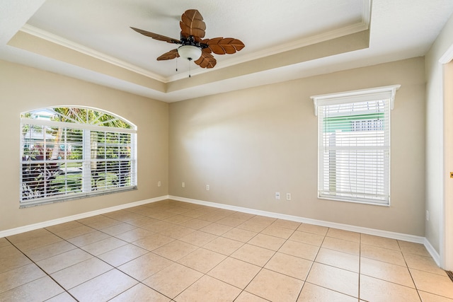 tiled empty room featuring ceiling fan, a wealth of natural light, and a tray ceiling